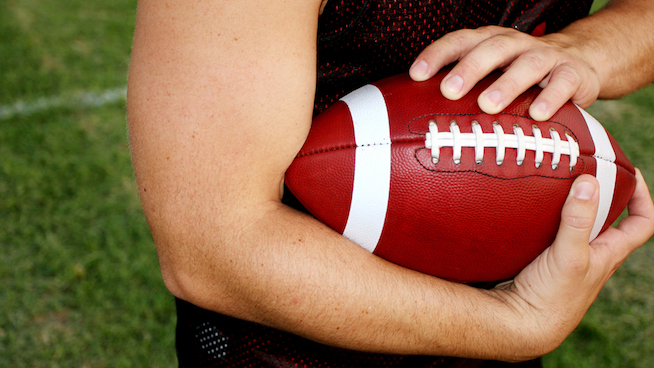 Close up of athlete holding an american football with tight grip while running on the football field