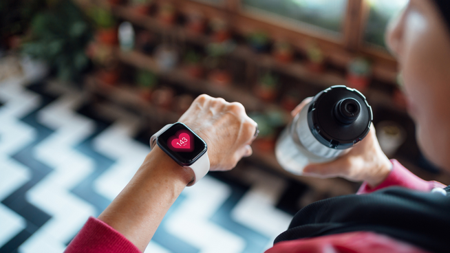 woman looking at smart watch with wellness app and holding water bottle