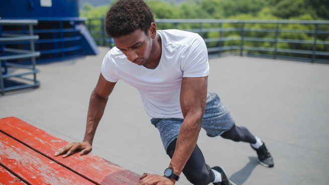 male athlete stretching hips outside at park on picnic table