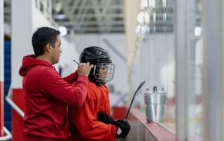 adult male helping young male hockey player with helmet